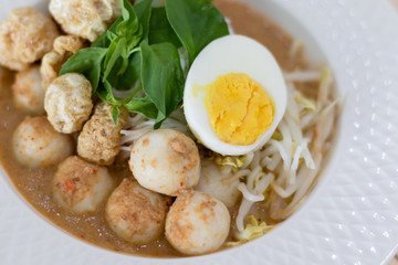 Thai Food. Rice Noodles in Fish Curry With boiled egg, fish balls, pork snack, basil, bean sprouts on top, placed on a wooden table.