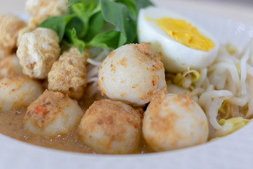 Thai Food Rice Noodles in Fish Curry With boiled egg, fish balls, pork snack, basil, bean sprouts on top, placed on a wooden table.