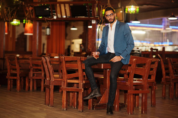 Fototapeta na wymiar Handsome well-dressed arabian man with glass of whiskey and cigar posed at pub.