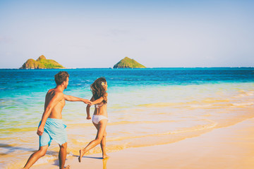 Beach couple happy in love having fun running on summer Hawaii vacation travel. Man and woman...