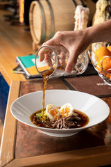 Pouring kvass in traditional russian summer soup okroshka with eggs and fresh vegetables