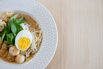 Thai Food. Rice Noodles in Fish Curry With boiled egg, fish balls, pork snack, basil, bean sprouts on top, placed on a wooden table.