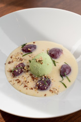 Close up of ice cream dessert with a scoop of pistachio ice cream, plums, almonds and creamy sauce as a fine dining meal