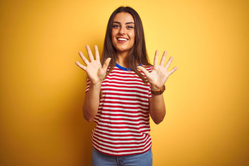 Young beautiful woman wearing striped t-shirt standing over isolated yellow background showing and pointing up with fingers number ten while smiling confident and happy.