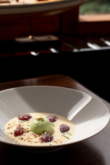 Fancy ice cream dessert with a scoop of pistachio ice cream, plums, almonds and creamy sauce, shot in a daylight