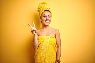 Young beautiful woman wearing towel after shower over isolated yellow background showing and pointing up with fingers number two while smiling confident and happy.