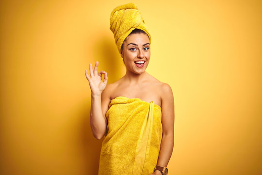 Young beautiful woman wearing towel after shower over isolated yellow background smiling positive doing ok sign with hand and fingers. Successful expression.