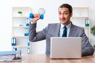 Young handsome employee doing sport exercises at workplace