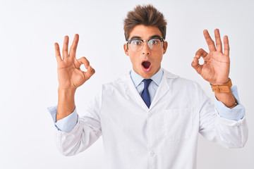 Young handsome sciencist man wearing glasses and coat over isolated white background looking surprised and shocked doing ok approval symbol with fingers. Crazy expression