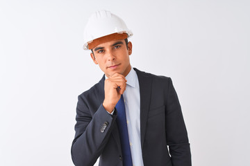 Young handsome architect man wearing suit and helmet over isolated white background looking confident at the camera smiling with crossed arms and hand raised on chin. Thinking positive.
