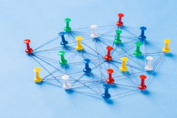 Small network of colorful pins and string, An arrangement of colorful pins linked together with string on a blue background suggesting a network of connections.