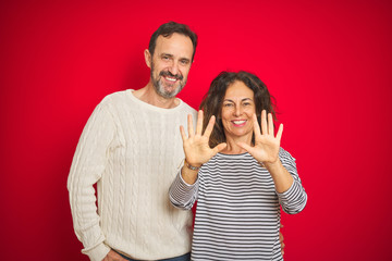 Beautiful middle age couple wearing winter sweater over isolated red background showing and pointing up with fingers number ten while smiling confident and happy.
