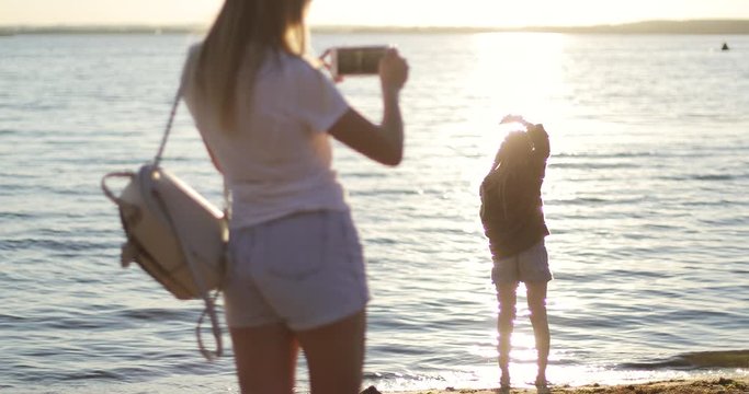Mom takes pictures of her daughter on the background of the sunset