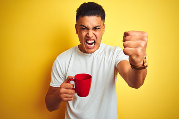 Young brazilian man drinking cup of coffee standing over isolated yellow background annoyed and...