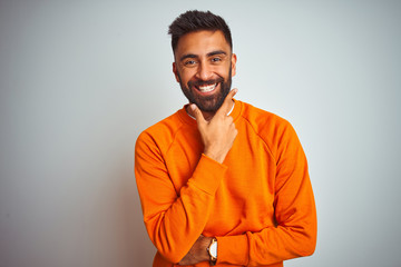 Fototapeta premium Young indian man wearing orange sweater over isolated white background looking confident at the camera smiling with crossed arms and hand raised on chin. Thinking positive.