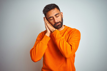 Young indian man wearing orange sweater over isolated white background sleeping tired dreaming and posing with hands together while smiling with closed eyes.