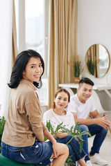 Pretty young Asian woman attending meeting with friends, sitting on sofa and turning back to camera