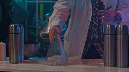 A man in a medical coat is mixing chemicals in a glass flask