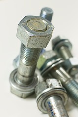 Stainless steel nuts and bolts on white background with strong defocus