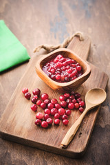 Cranberry jam in a wooden bowl on a wooden background.