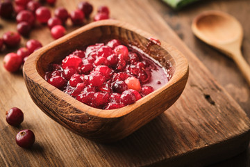 Cranberry jam in a wooden bowl on a wooden background.