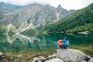 hikers couple sitting on rock looking at lake in mountains