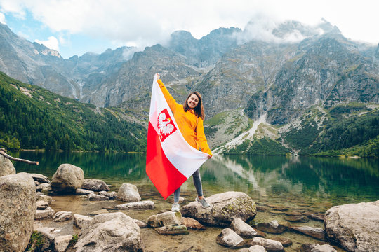 young pretty smiling woman holding poland flag at beach of mountain lake