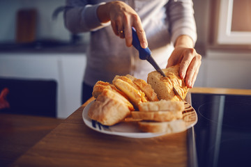 Close up of caucasian housewife slicing bread while standing in kitchen at home. Breakfast preparation concept.