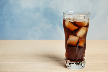 Glass of refreshing soda drink on wooden table against blue background, space for text