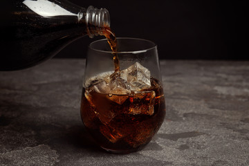 Pouring refreshing soda drink into glass on grey table