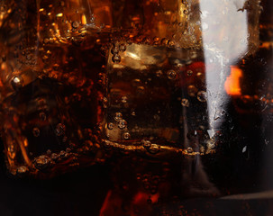 Glass of refreshing soda drink with ice cubes as background, closeup