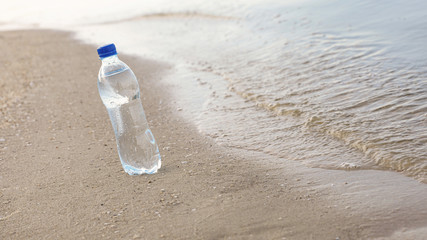 Fototapeta na wymiar Plastic bottle with refreshing drink on sandy beach near sea, space for text. Hot summer day