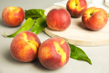 Tasty fresh peaches, leaves and stone board on grey table