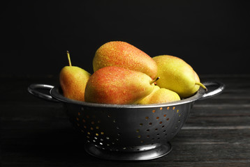 Colander with pears on dark wooden table against black background