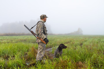 a hunter and his gundog are in a meadow on a foggy morning