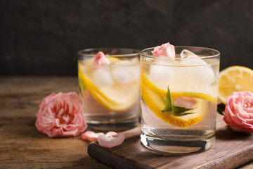 Delicious refreshing drink with lemon and roses on wooden table