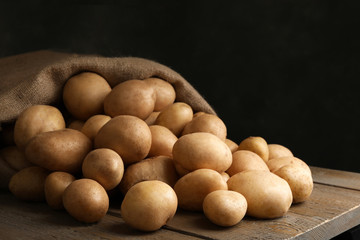 Raw fresh organic potatoes on wooden table against dark background