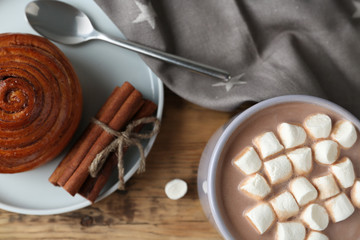 Composition with delicious hot cocoa drink and bun on wooden background, flat lay