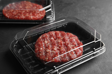 Plastic containers with raw meat cutlets for burger on grey table
