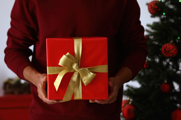 Man in red sweater holding Christmas gift at home, closeup