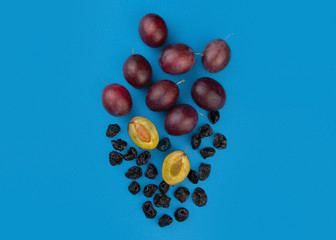 Fresh ripe plums, whole and halves, and dried prunes on a blue background.