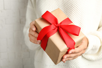 Young woman holding Christmas gift on light background, closeup