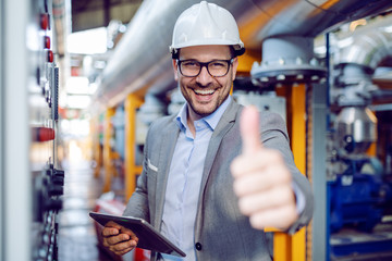 Successful caucasian supervisor in suit and with helmet holding tablet and showing thumbs up while...