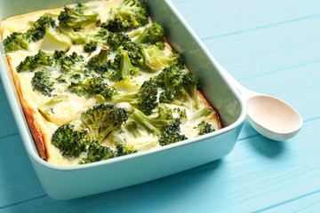 Tasty broccoli casserole in baking dish on blue wooden table