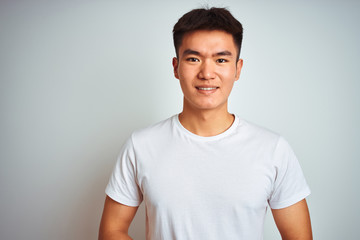 Young asian chinese man wearing t-shirt standing over isolated white background with hands together and crossed fingers smiling relaxed and cheerful. Success and optimistic