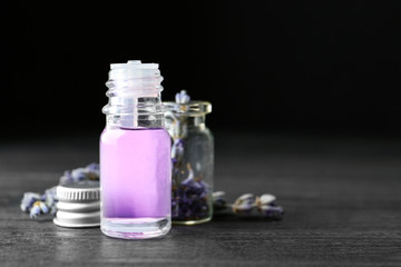 Bottles of natural essential oil and lavender flowers on dark wooden table. Space for text