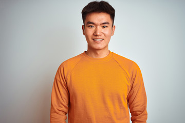 Young asian chinese man wearing orange sweater standing over isolated white background with a happy and cool smile on face. Lucky person.
