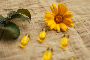 Obraz na płótnie Canvas Close up yellow calendula flower at linen fabric with blurred fish oil capsules and raspberry leaf, soft focus