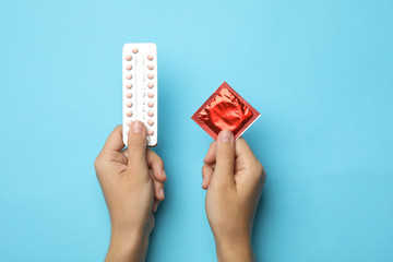 Woman holding condom and birth control pills on blue background, top view. Safe sex