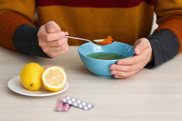 Sick young man eating soup to cure flu at table